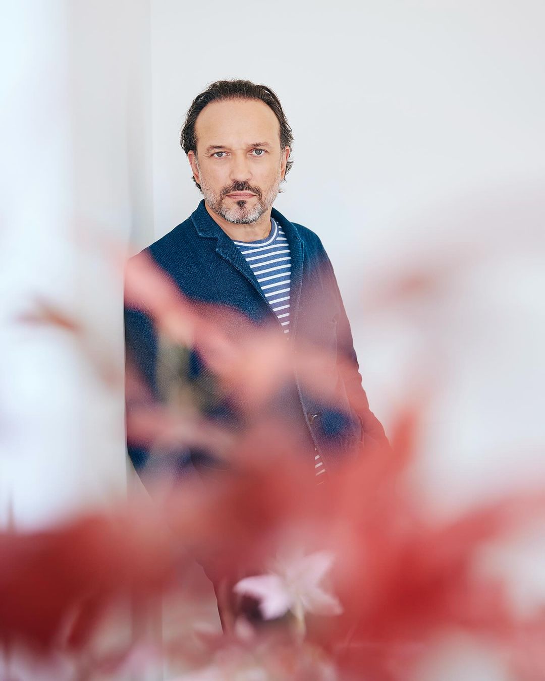 Portrait of a middle-aged man with dark hair and a beard, wearing a blue jacket and striped shirt, posing indoors with a soft background.