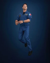Man in a blue flight suit with patches floating against a dark blue background by photographer Audoin Desforges