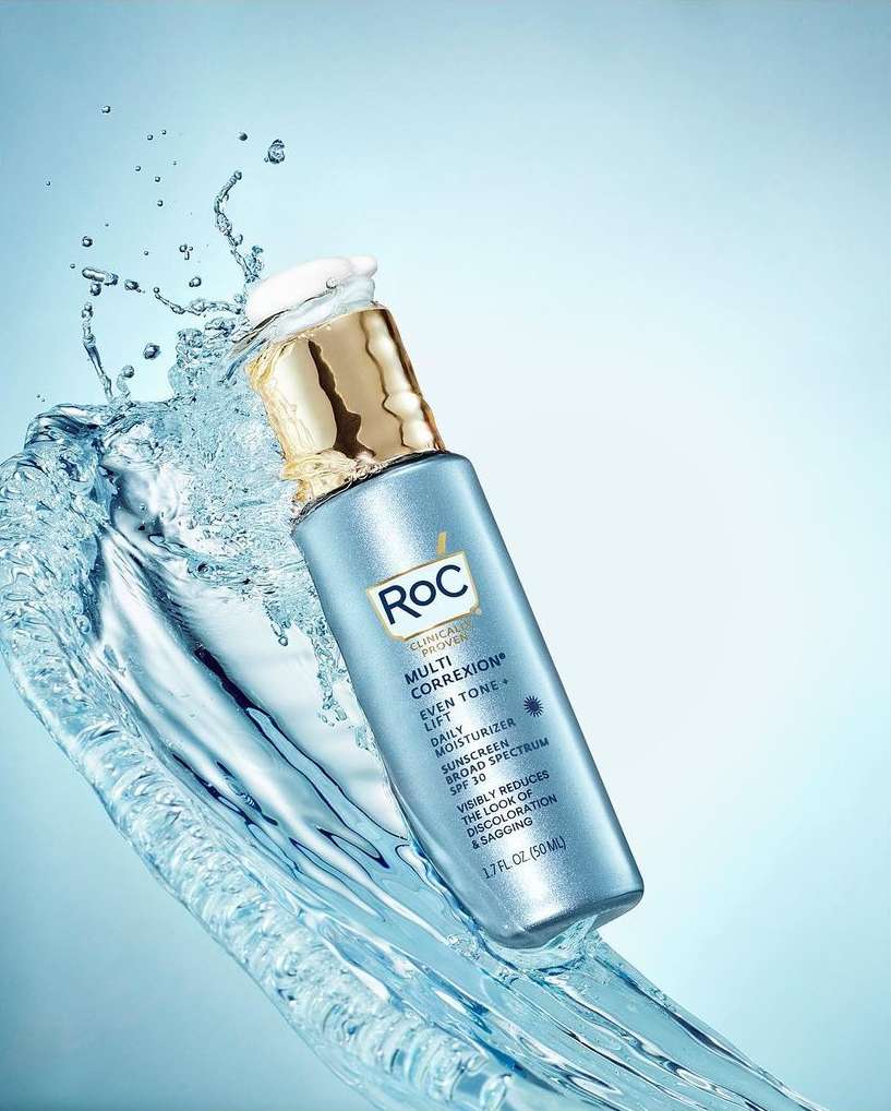 RoC Multi Correxion Even Tone + Lift product shot in studio with water splash effect against soft blue gradient background. Beauty advertising.