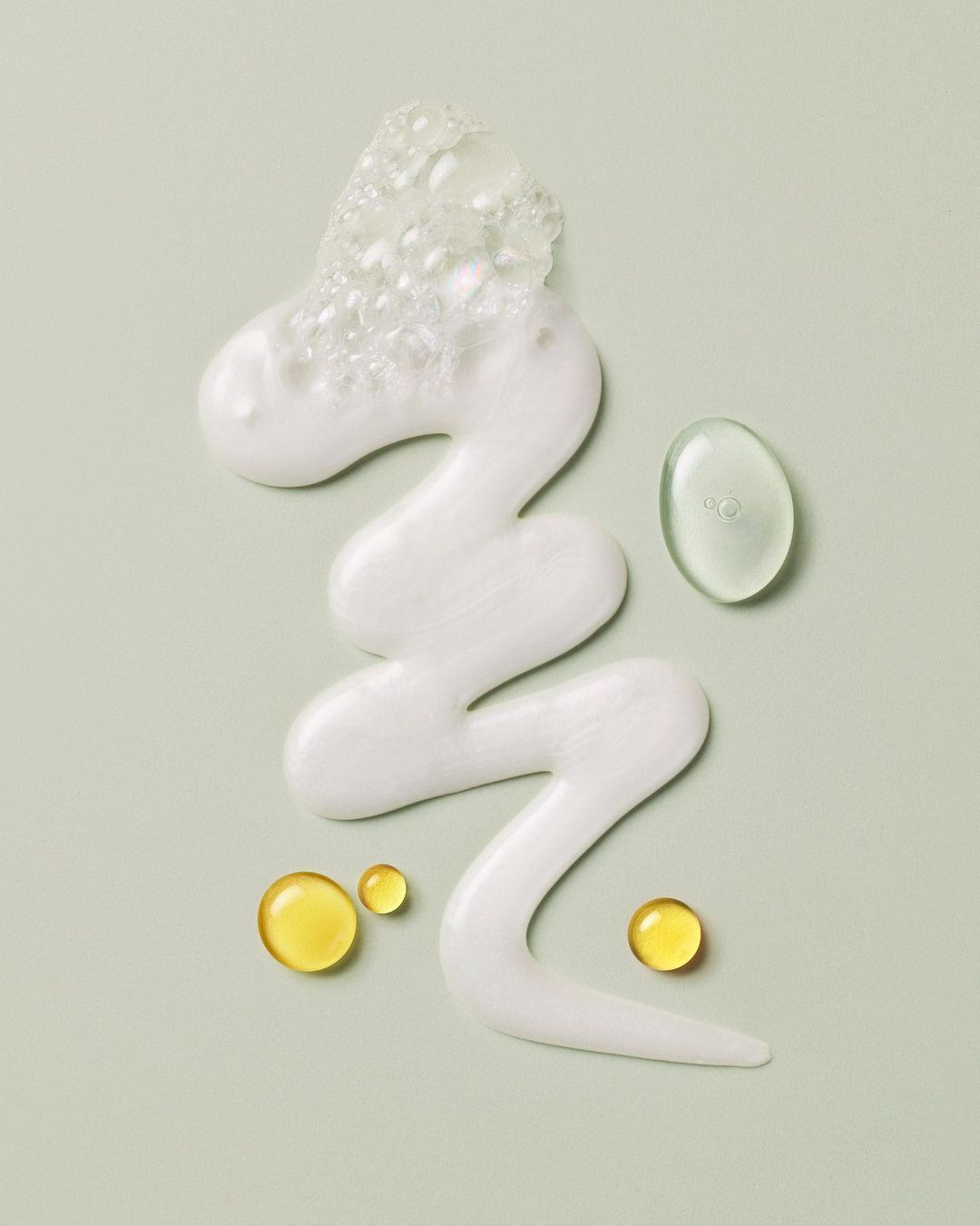 White and transparent cosmetic cleanser product with yellow and green drops on a light green background for beauty and healthcare campaigns.