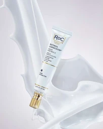 White skincare product tube angled amidst fluid white splashes against a pale backdrop