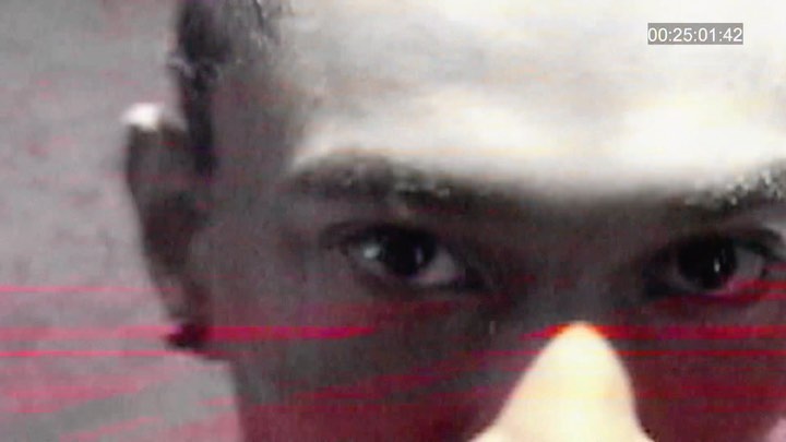 Extreme close-up of a Black adult's face focusing on their eye, nose, and part of their forehead with red and gray color grading.