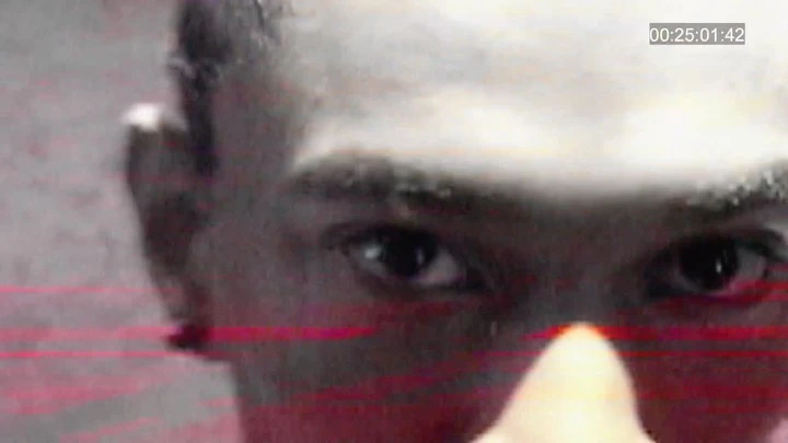 Extreme close-up of a Black adult's face focusing on their eye, nose, and part of their forehead with red and gray color grading.