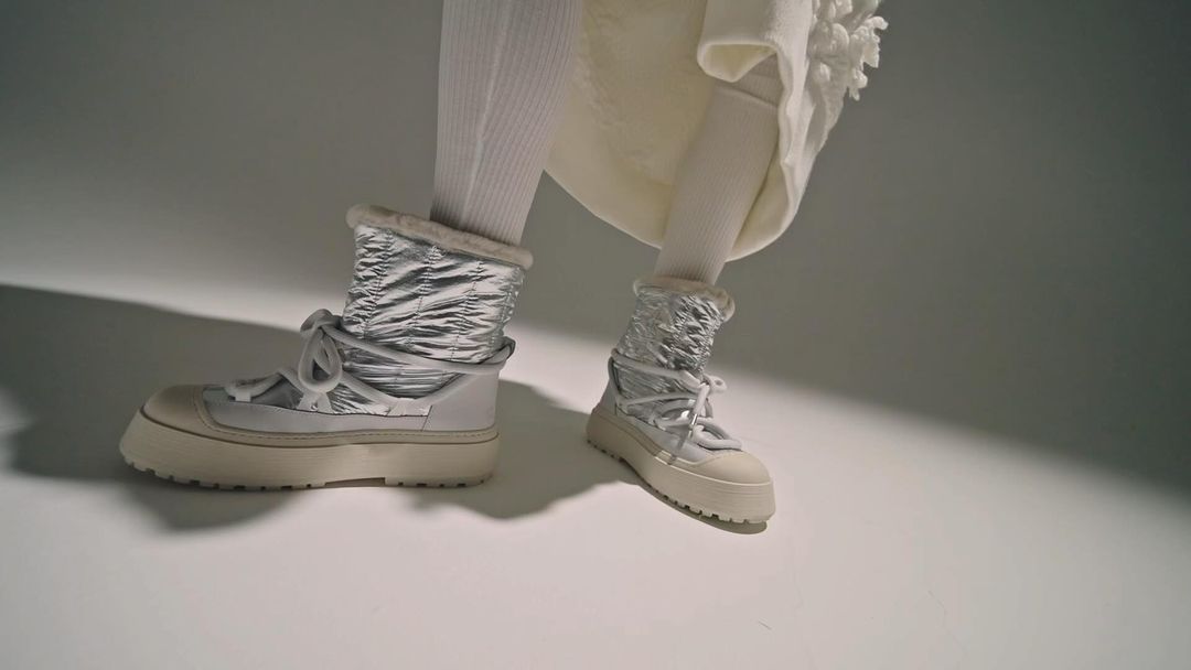 Fashion shot: Person wearing metallic silver puffer boots with cream laces and thick sole, paired with white socks and a dress.