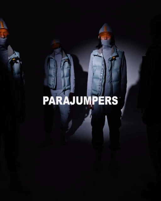Four fashion models stand in a dimly lit studio wearing puffer vests, turtlenecks, and matching knit caps, showcasing winter outerwear.