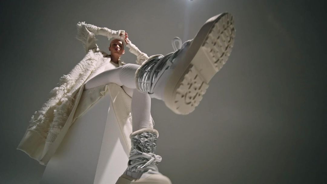 Fashionable woman wearing all white and Moon Boots. Worm's eye view perspective of silver Moon Boots with white platform sole.