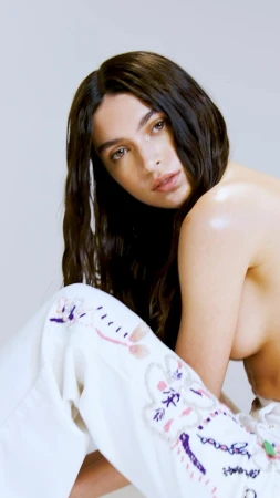 Portrait of a woman with long dark hair wearing white embroidered trousers against a plain background