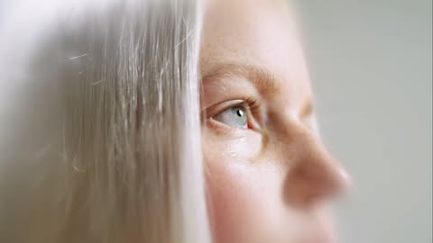Close-up portrait of an adult female with blue eyes and platinum blonde hair, looking upward against a soft, blurred background.