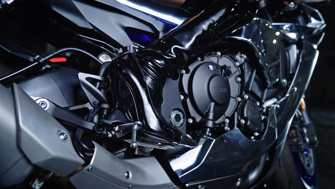 Motorcycle detail shot with a sleek, black design, showcasing the engine and frame with a rider wearing shiny black latex-like pants.