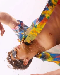 Close-up portrait of a man wearing dark sunglasses and a vibrant colorful patterned shirt surrounded by water splashes.