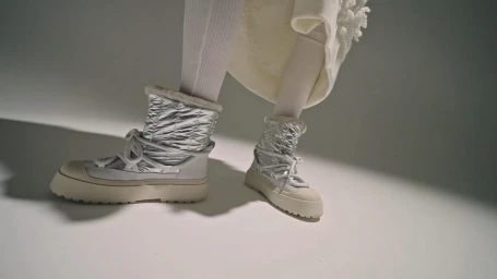 Close-up of silver metallic puffer snow boots and white ribbed tights against a plain studio background.