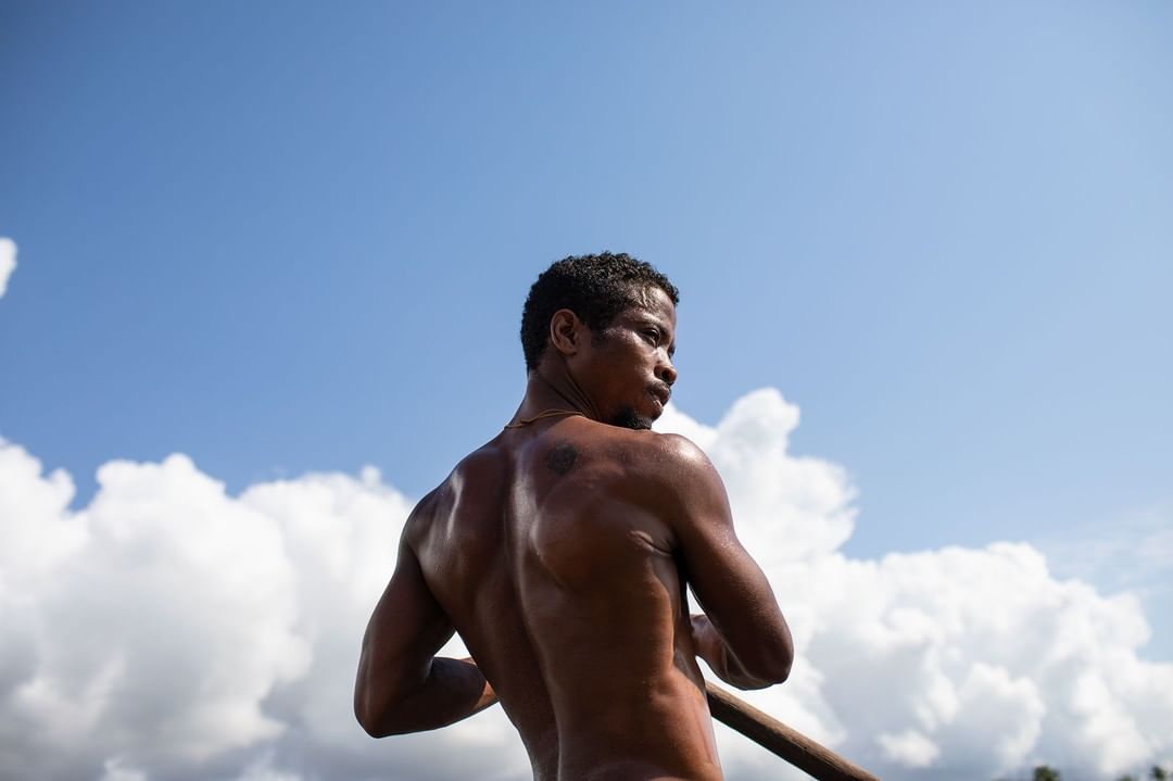 Low angle of shirtless man paddling on water under bright sky with clouds. Outdoor activity, blue skies, waterscape, male portrait.