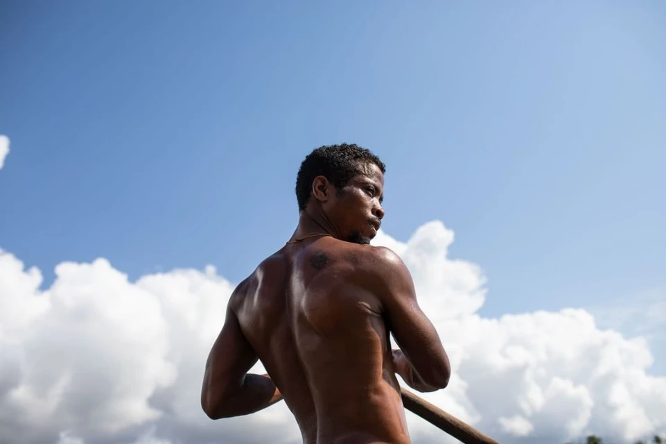Low angle of shirtless man paddling on water under bright sky with clouds. Outdoor activity, blue skies, waterscape, male portrait.