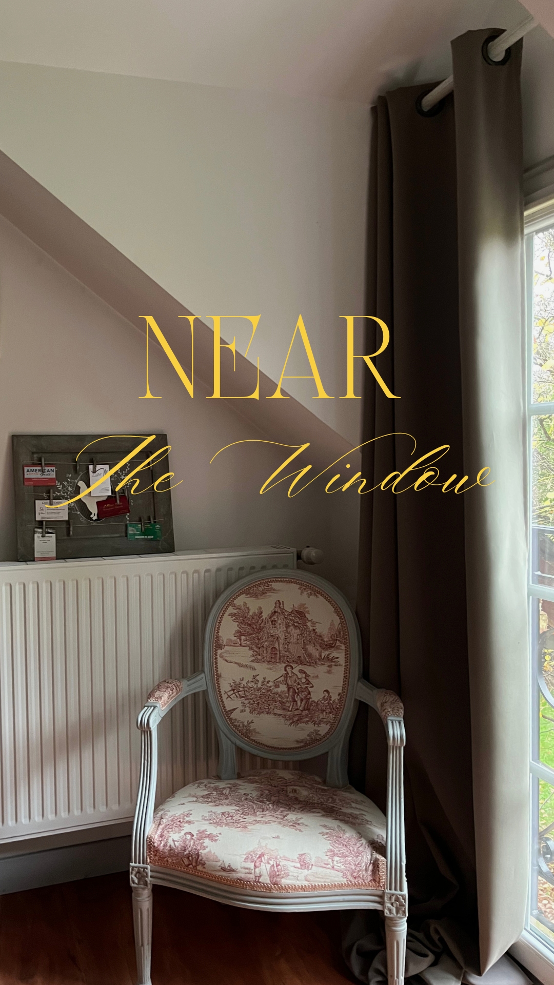 Interior view of a vintage-style chair with red toile fabric near a window with a curtain, radiator, and a small notice board.
