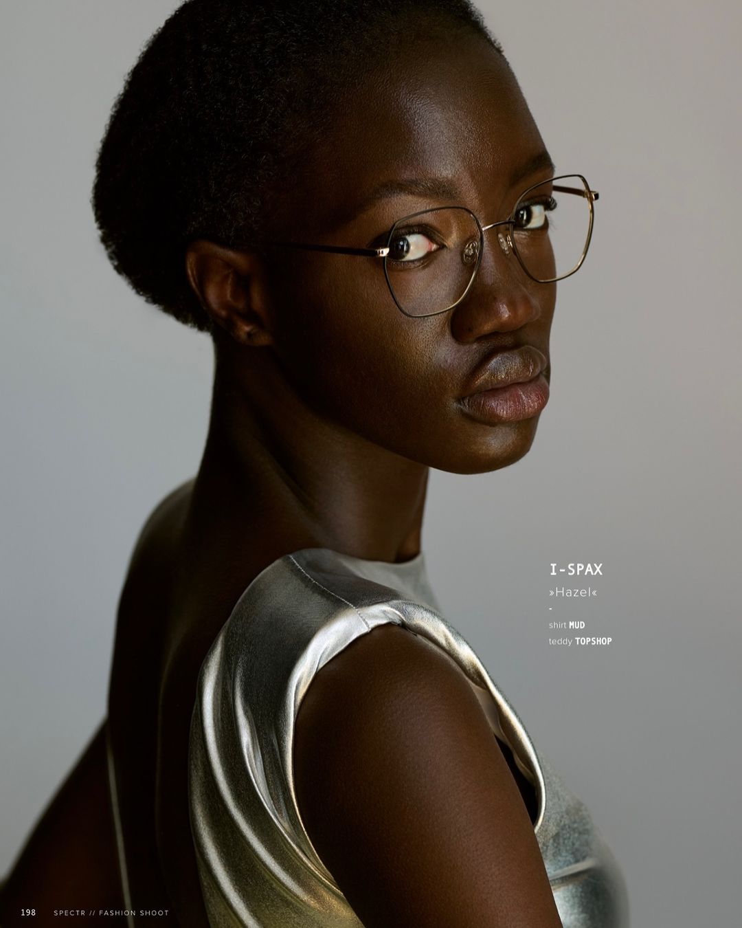 Close-up studio portrait of an African American woman with short black hair and wearing eyeglasses looking over her shoulder.