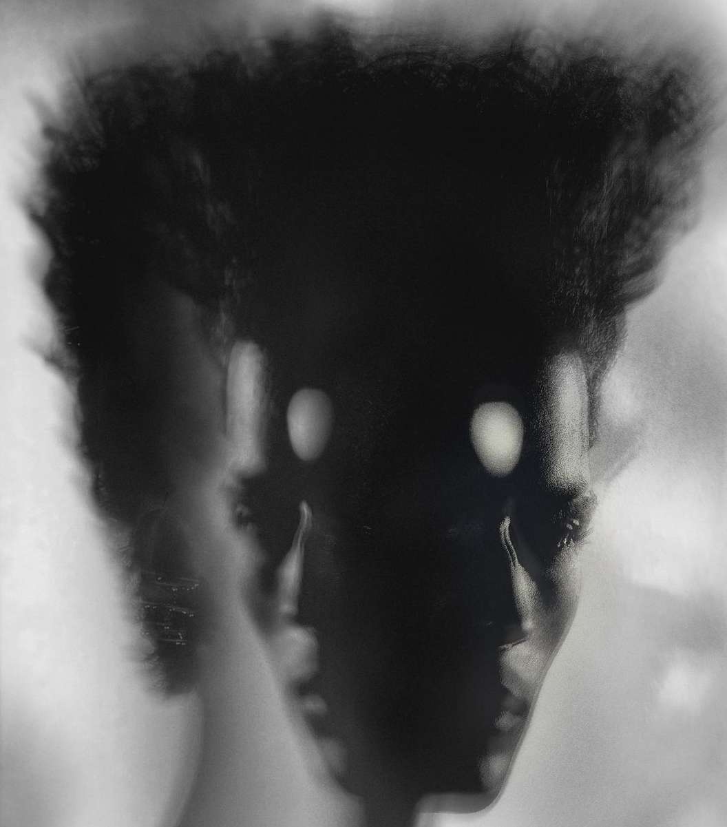 Monochromatic portrait of a Black woman with dark curly hair, featuring diffused lighting and a soft-focus background.