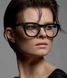 Close up portrait of a short-haired model wearing thick black frame eyeglasses against a grey background