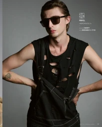 Man wearing dark sunglasses, distressed black tank top, and black overalls against a grey background in Munich by Ava Pivot.