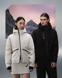 Two models standing in front of a mountain landscape backdrop, wearing technical outdoor jackets and apparel.