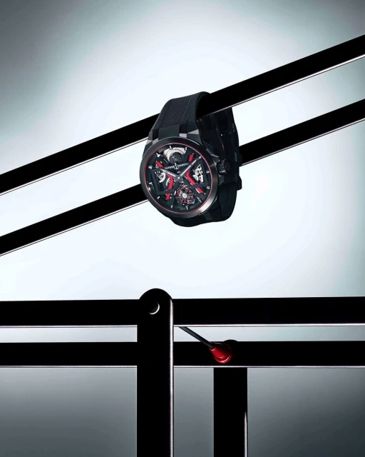 Luxury black Ulysse Nardin watch with red accents suspended by black rods on a white gradient background in a studio shot.