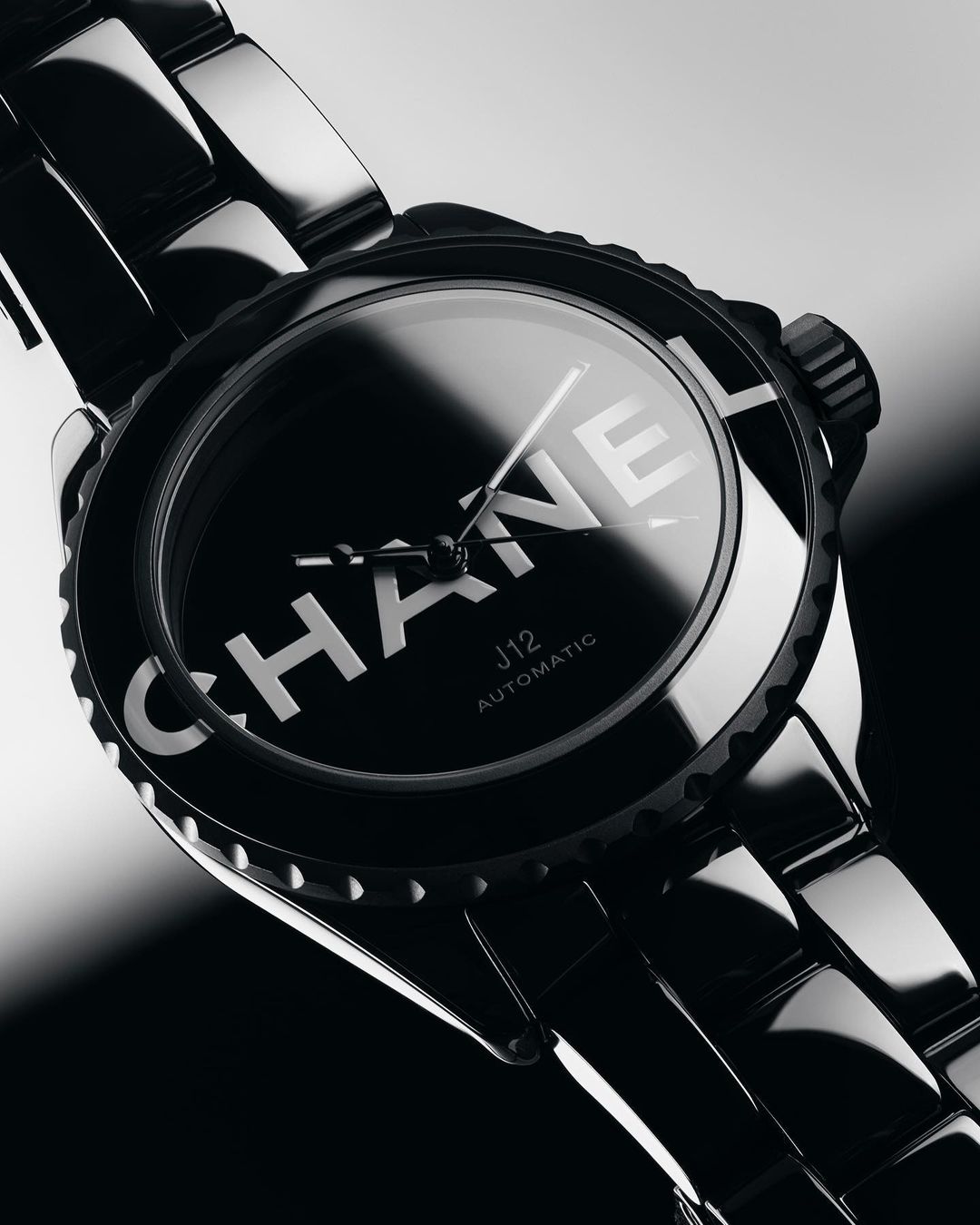 Close-up of a black Chanel J12 automatic watch with a glossy black bracelet and bezel, showcasing the brand name on the dial.