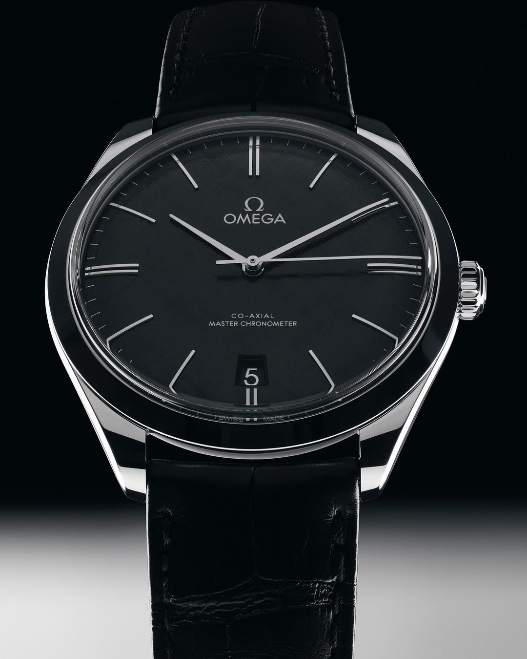 Omega wristwatch close-up against dark background. Stylish black leather band and silver case. Black dial with silver hands.