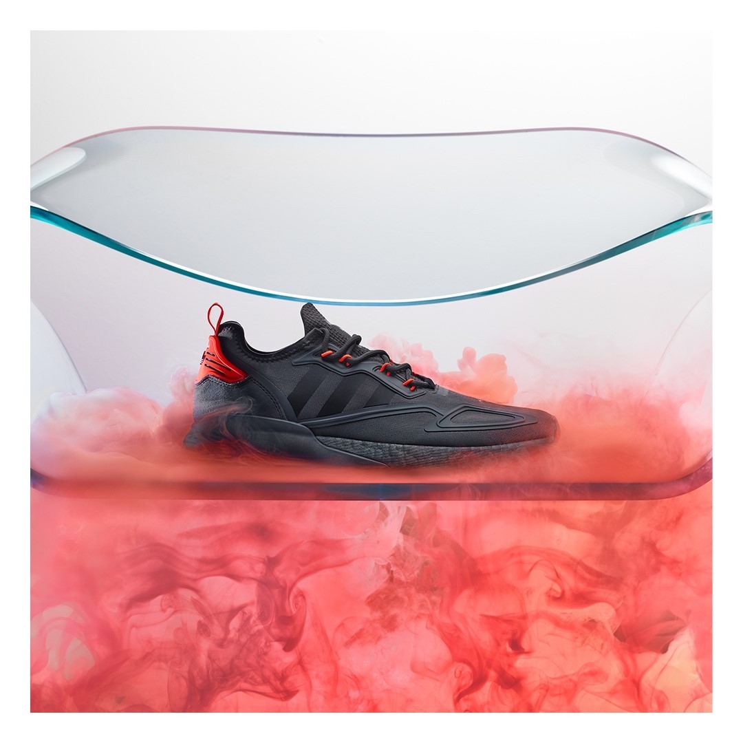 Adidas ZX 2K Boost sneaker on a clear platform surrounded by pink smoke, set against a bright white background in a product shot.
