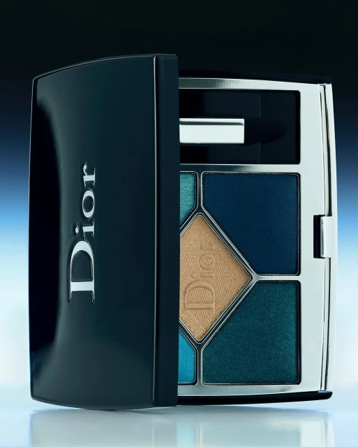 Dior eyeshadow palette with blue, gold, and teal shadows in geometric shapes, in a black and silver case, beauty product shot.