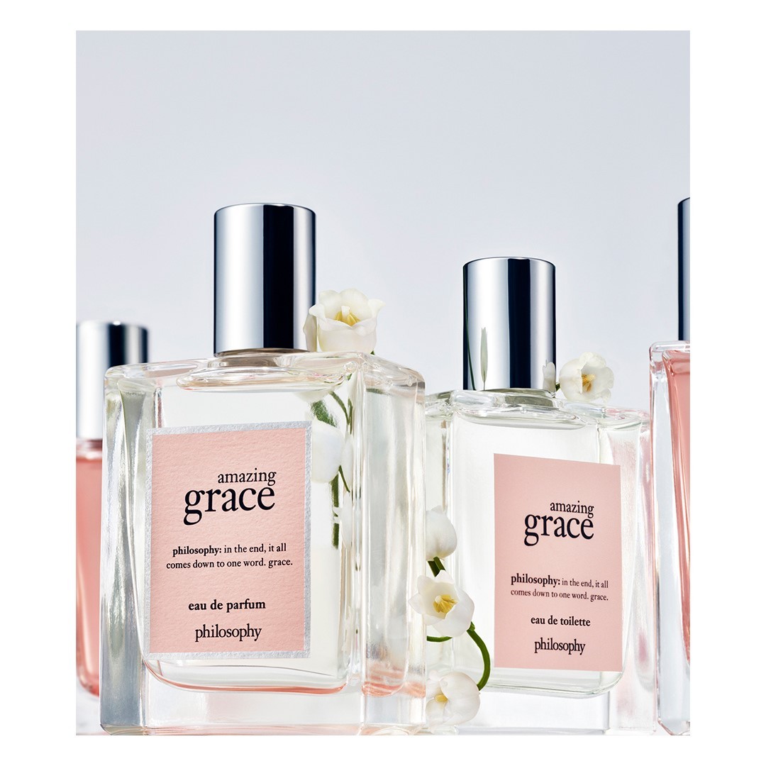 Close-up of several perfume bottles of Philosophy's Amazing Grace with transparent square bottles and silver caps, adorned with white flowers.
