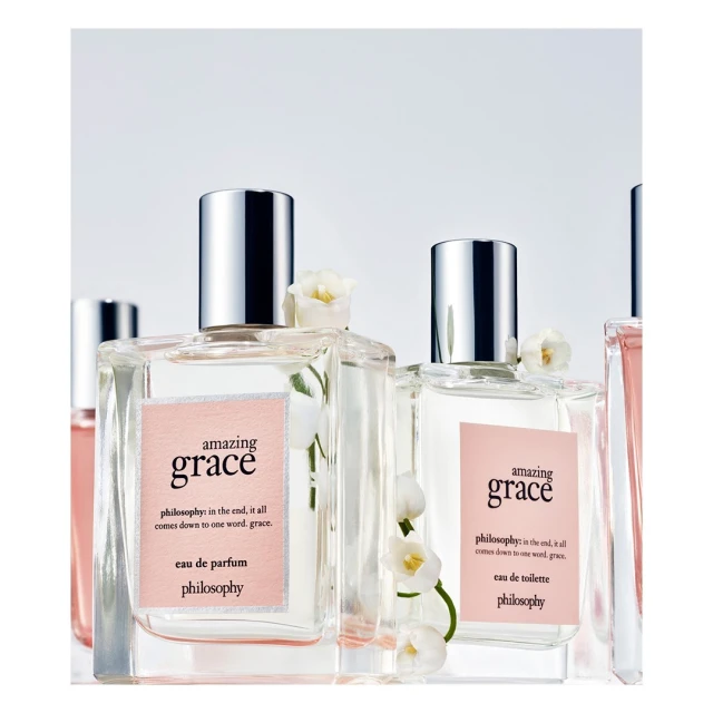 Close-up of several perfume bottles of Philosophy's Amazing Grace with transparent square bottles and silver caps, adorned with white flowers.