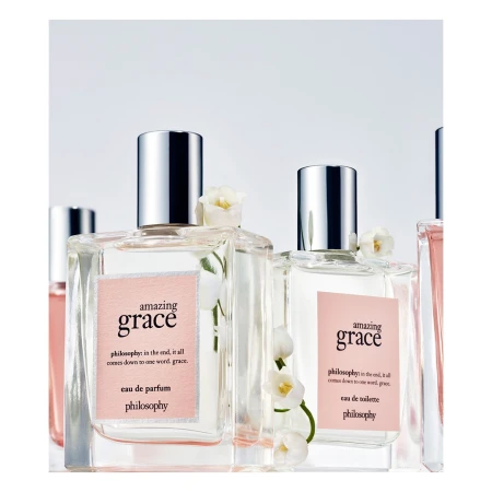 Close-up of several perfume bottles of Philosophy's Amazing Grace with transparent square bottles and silver caps, adorned with white flowers.