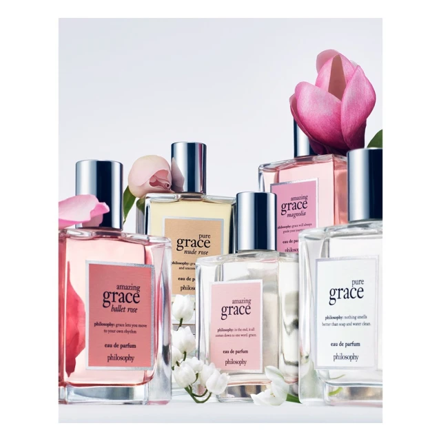 Several Philosophy fragrance bottles are arranged with pink and white flowers against a bright white backdrop. Beauty and personal care product shot.