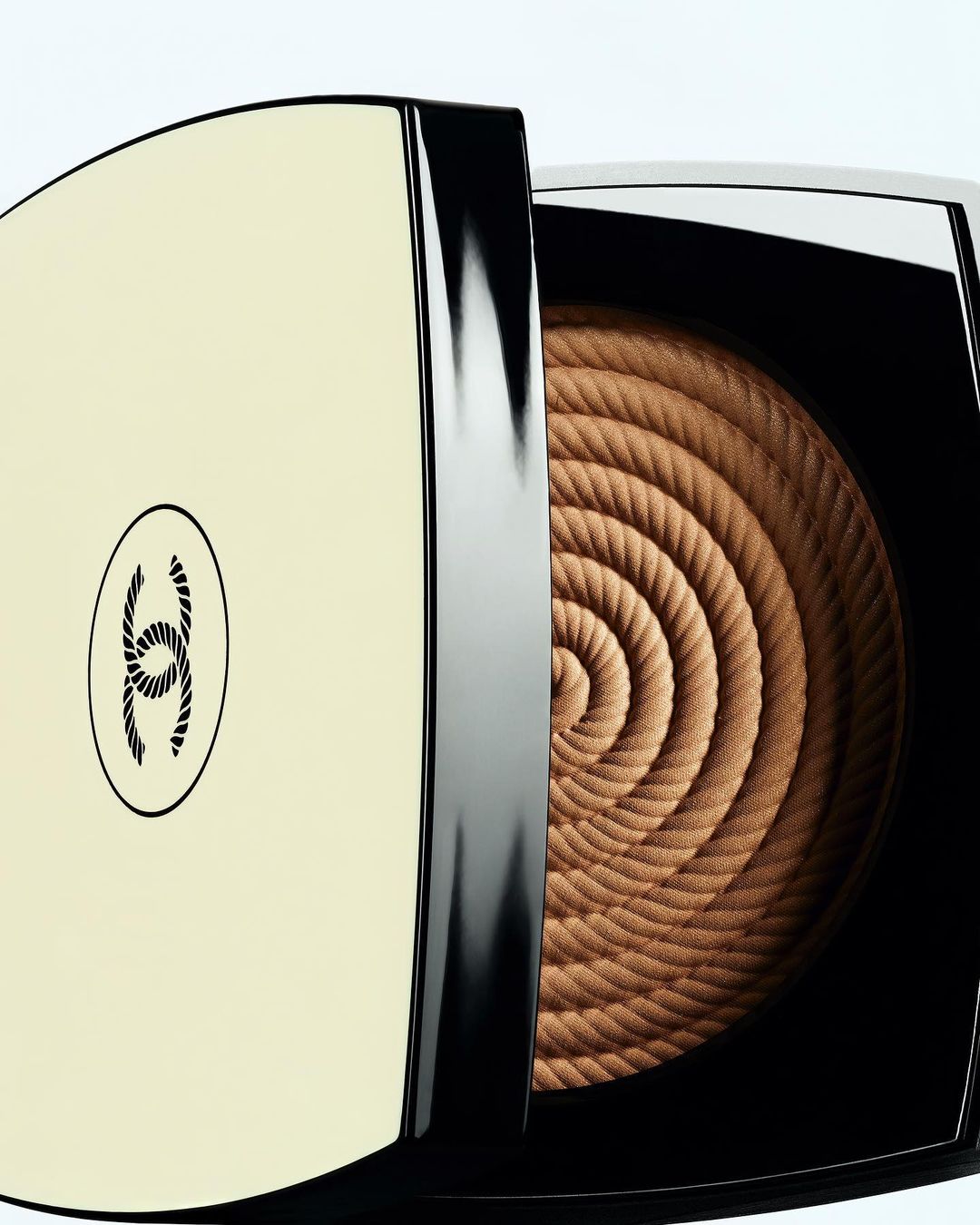 Close-up of bronzer makeup with spiral rope pattern in a square compact case featuring the Chanel logo on a white background.