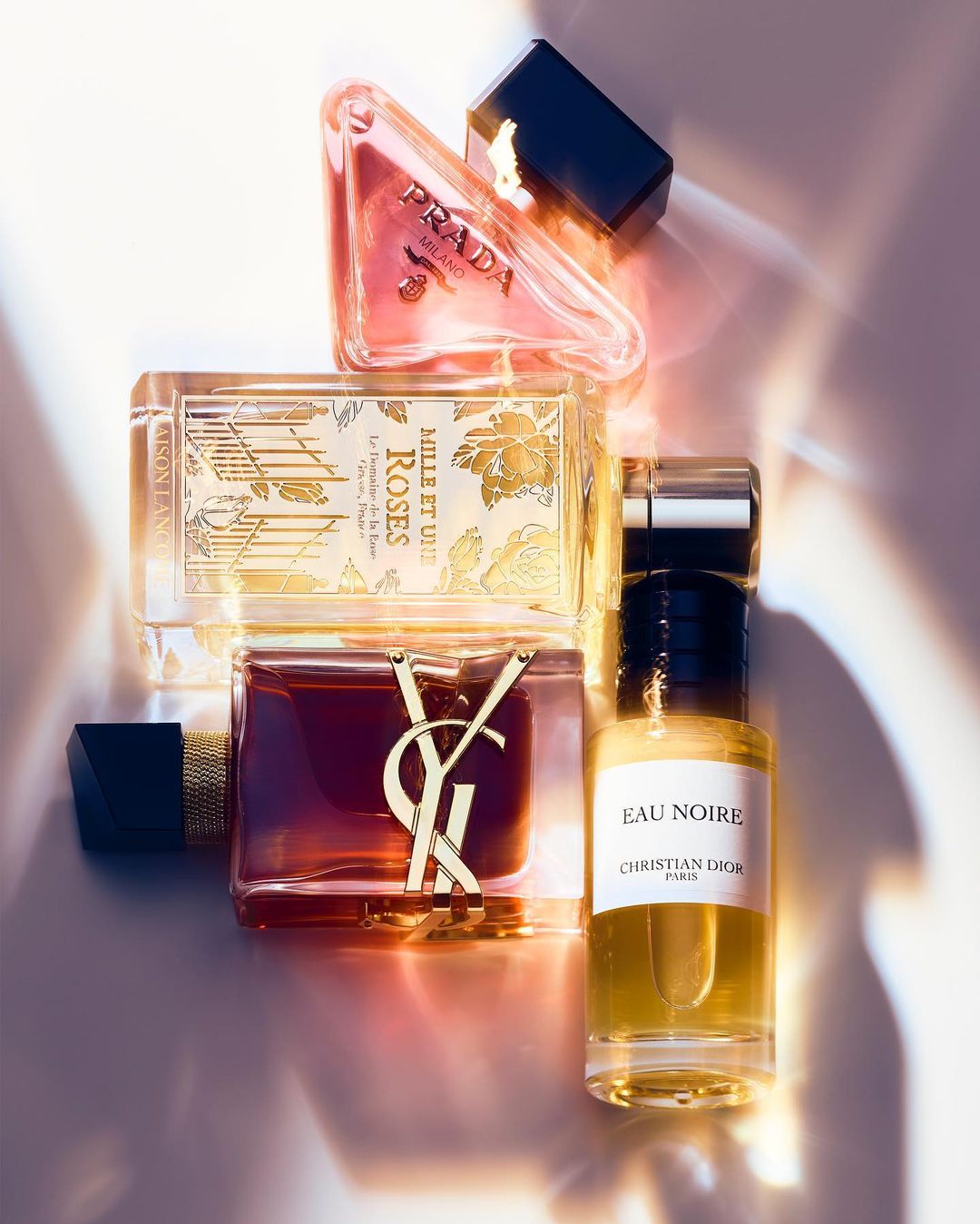 Still life shot of Prada, Yves Saint Laurent, Christian Dior, and other perfume bottles with black caps and various shapes and sizes.
