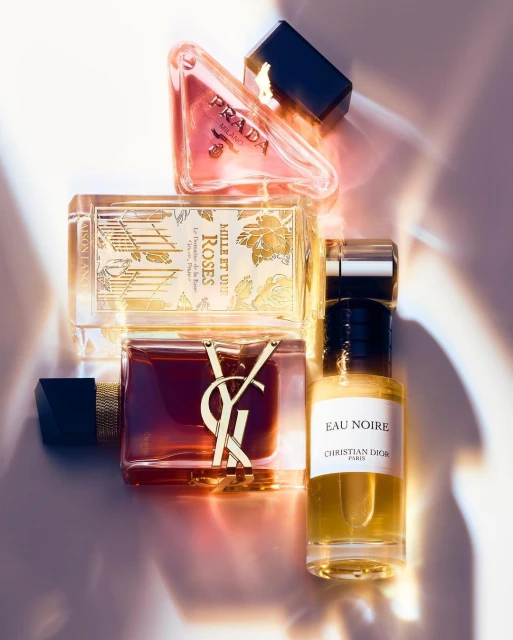Still life shot of Prada, Yves Saint Laurent, Christian Dior, and other perfume bottles with black caps and various shapes and sizes.