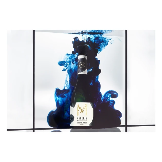 Studio shot of a wine bottle engulfed in swirling blue liquid, set against a minimalist grid backdrop, showcasing artistic food and beverage product photography.