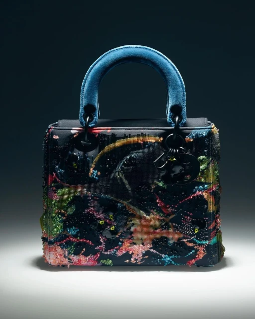 Elegant black Dior Lady handbag with colorful floral embroidery and a blue handle, displayed against a dark, smooth backdrop.