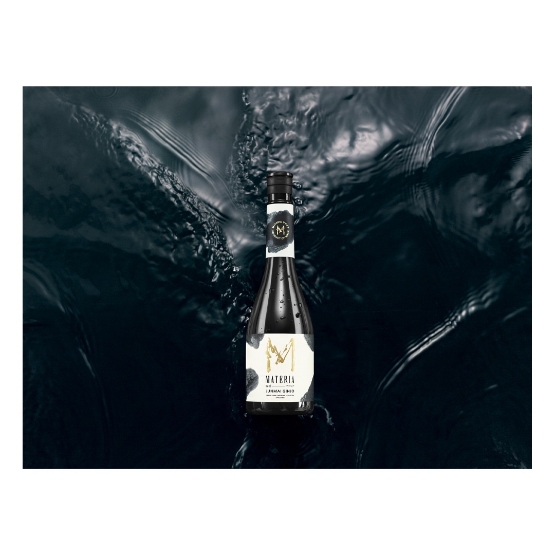 A sleek bottle of Materia skincare floats atop the dark, rippling surface of the water, with the brand logo prominently displayed.