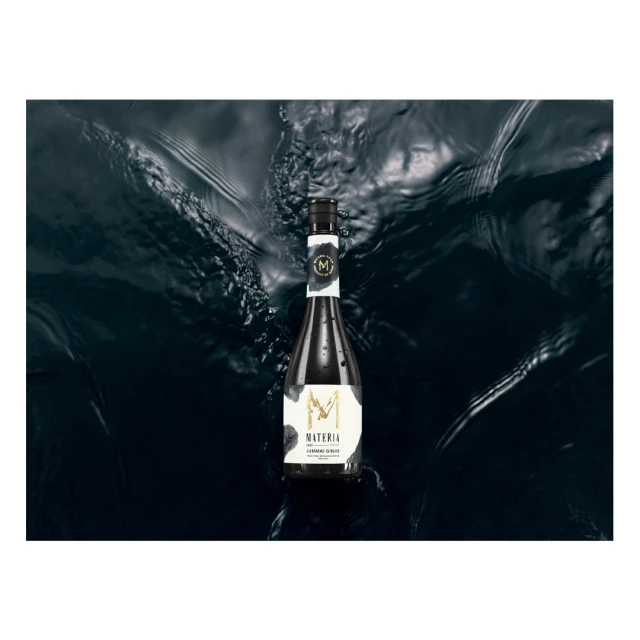 A sleek bottle of Materia skincare floats atop the dark, rippling surface of the water, with the brand logo prominently displayed.