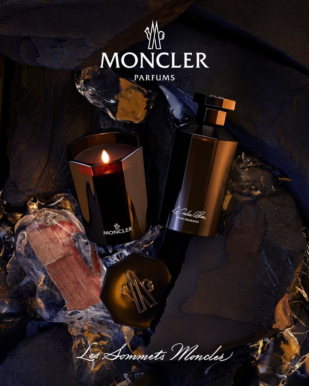 Moncler fragrance and candle on dark textural surface with logo. Perfume bottle and candle present brand in product shot.