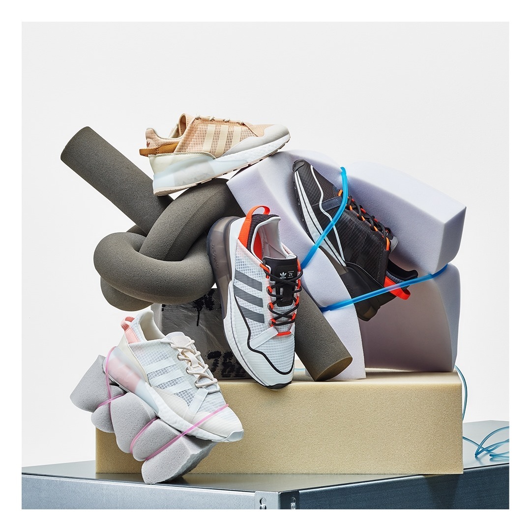 Several Adidas brand sneakers of different colors and designs are arranged on top of foam blocks in a studio setting.