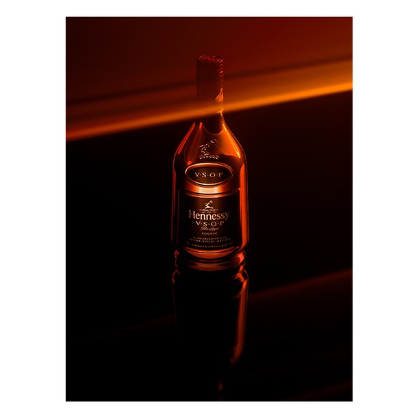 Hennessy VSOP cognac bottle is displayed in a studio, spotlighted with a reflective surface, and soft, amber lighting.