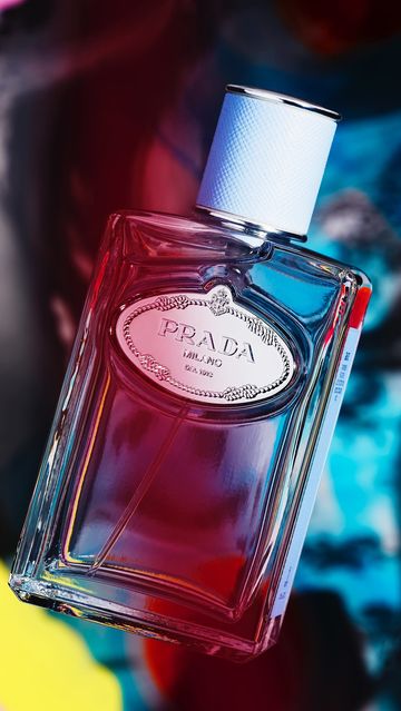 Prada perfume bottle close-up on a vibrant background of red, blue, and yellow, showcasing its clear glass and light blue accents.