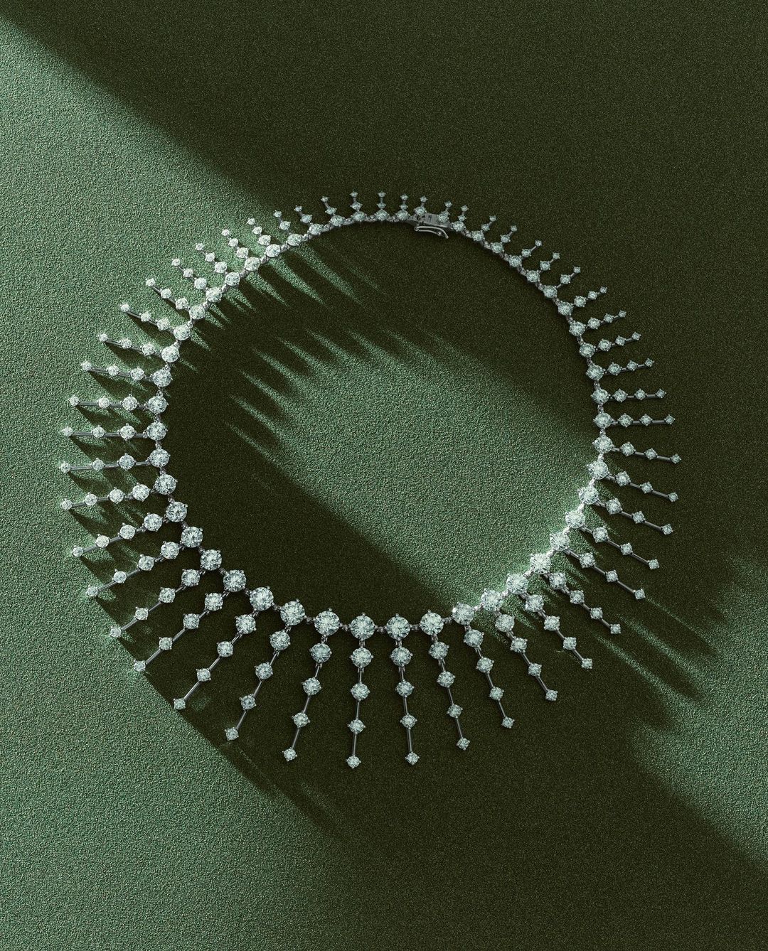 Diamond necklace on a green textured surface with strong directional light casting shadows. Jewelry for fashion, luxury, and elegance.