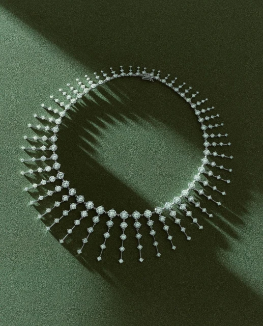 Diamond necklace on a green textured surface with strong directional light casting shadows. Jewelry for fashion, luxury, and elegance.