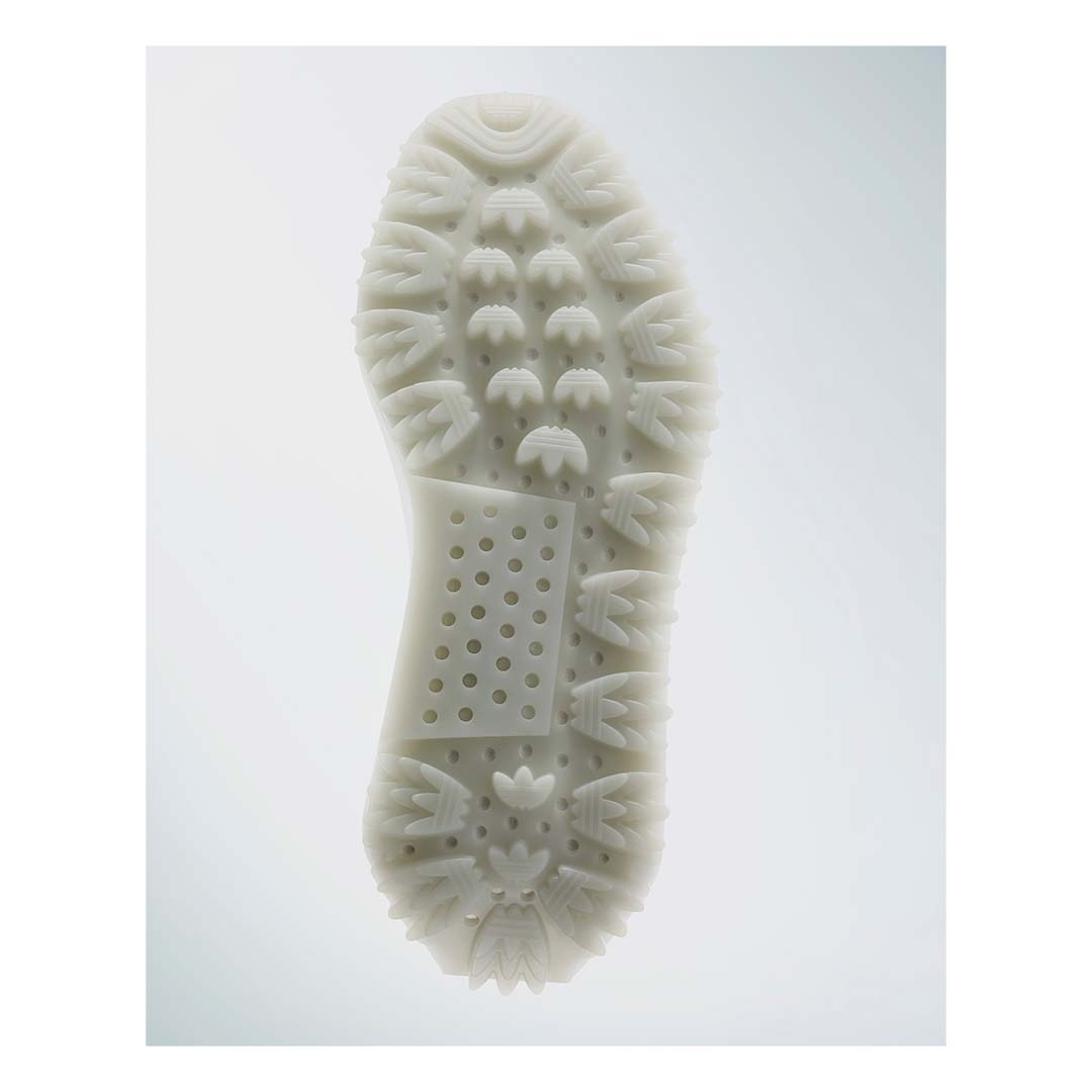 Close-up studio shot of the textured sole of a white shoe with circular and ridge patterns, highlighting the design and grip.