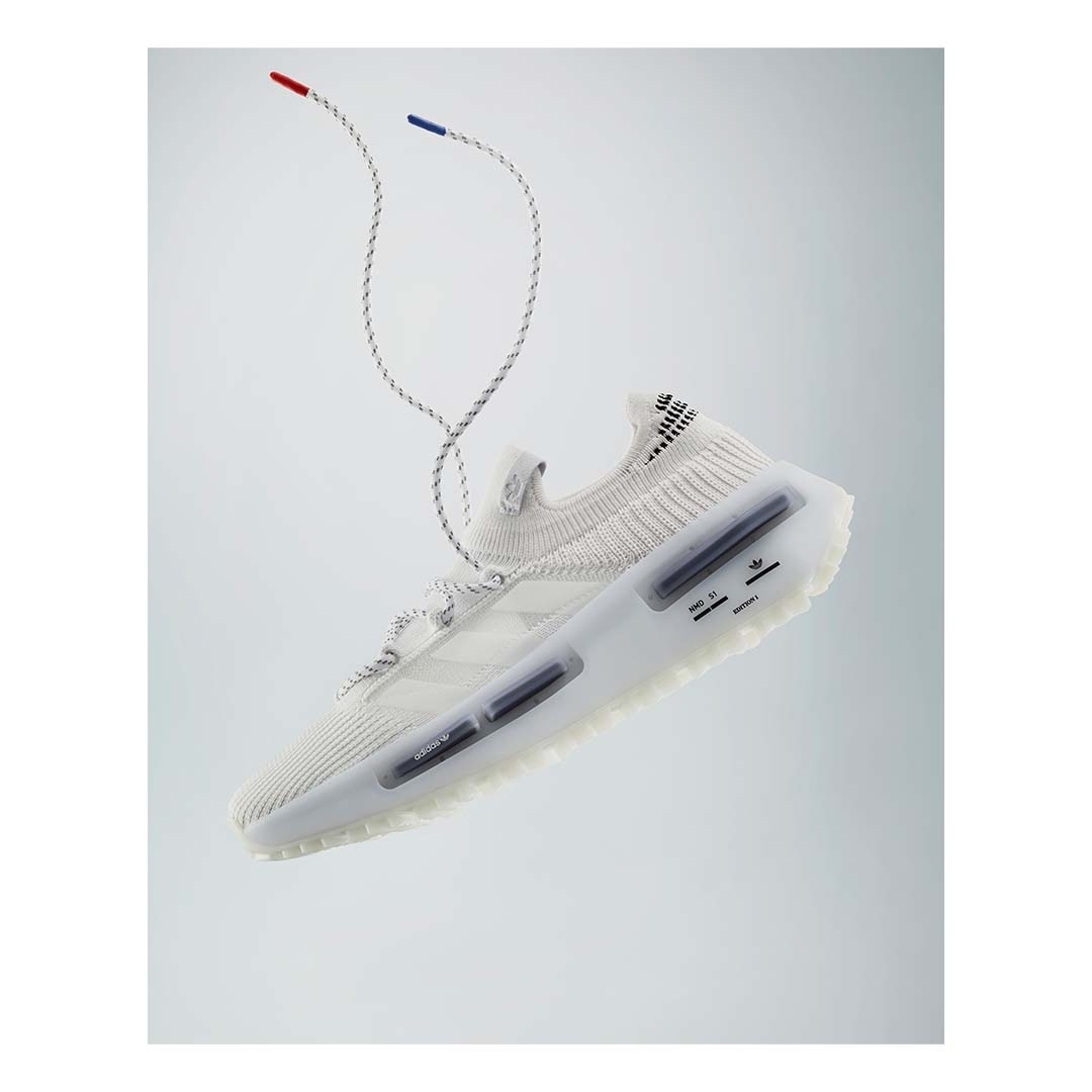 Studio shot of a white Adidas running shoe with patterned laces featuring red and blue tips, set against a bright white background.