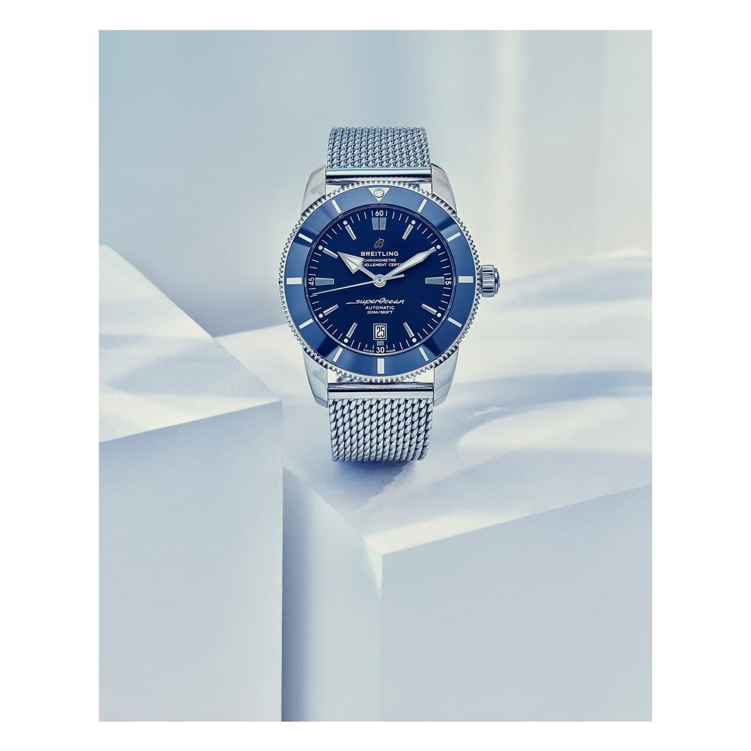 Luxury Breitling Superocean watch featuring a blue dial and silver mesh strap, elegantly displayed on a geometric white surface.