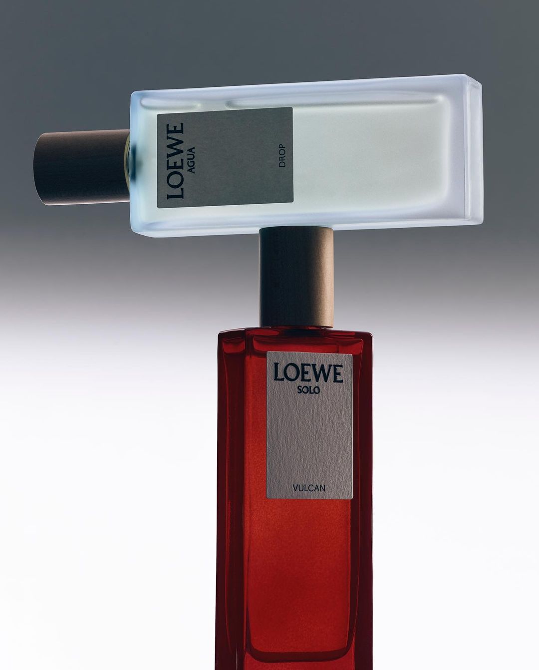 Two perfume bottles balanced vertically with a frosted white glass bottle resting horizontally on top of a tall red glass bottle.