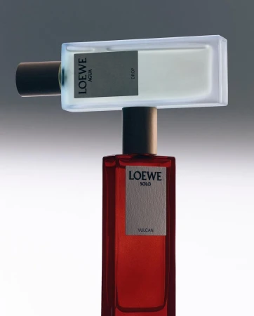 Two perfume bottles balanced vertically with a frosted white glass bottle resting horizontally on top of a tall red glass bottle.